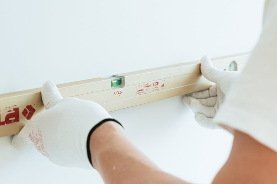 Hands in white gloves using spirit level on wall for precise leveling.